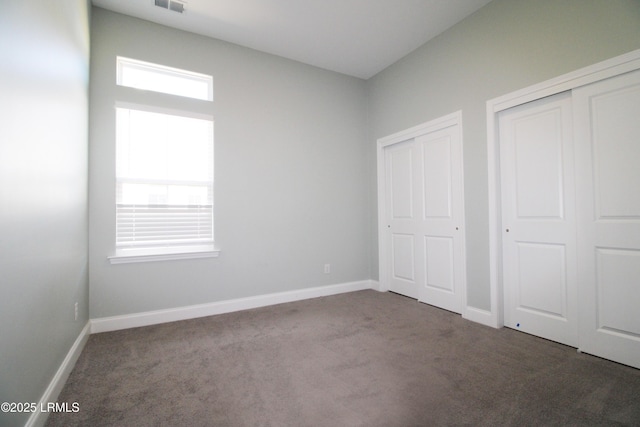 unfurnished bedroom with multiple closets, visible vents, baseboards, and carpet flooring