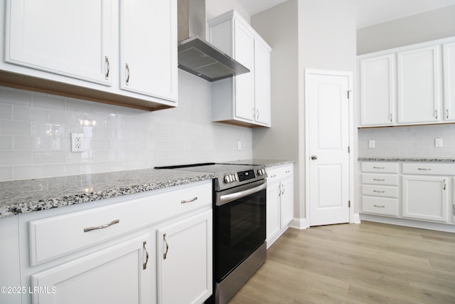 kitchen featuring light stone counters, light wood finished floors, white cabinets, wall chimney range hood, and stainless steel range with electric stovetop