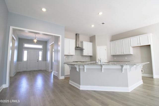 kitchen with wall chimney range hood, a large island, visible vents, and white cabinets