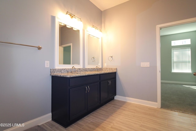 full bathroom featuring double vanity, baseboards, a sink, and wood finish floors