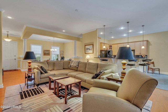 living room featuring an inviting chandelier, ornamental molding, light hardwood / wood-style flooring, and ornate columns