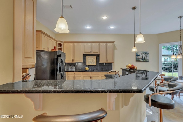 kitchen featuring light brown cabinetry, hanging light fixtures, black fridge with ice dispenser, and backsplash