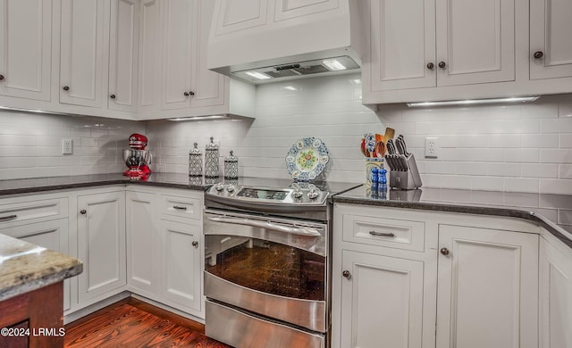 kitchen with white cabinetry, stainless steel electric range oven, dark hardwood / wood-style floors, range hood, and backsplash