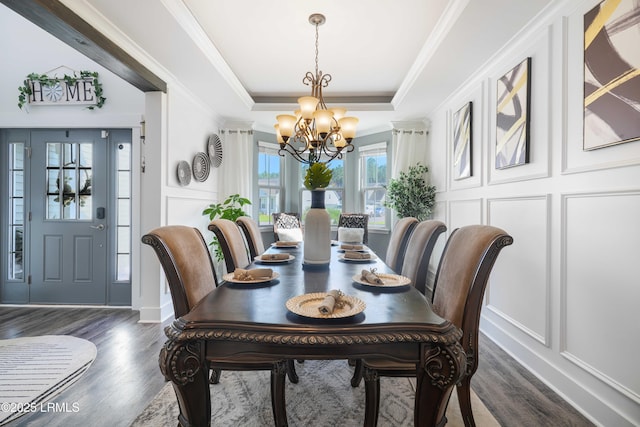 dining area featuring a raised ceiling, ornamental molding, dark wood-type flooring, and an inviting chandelier