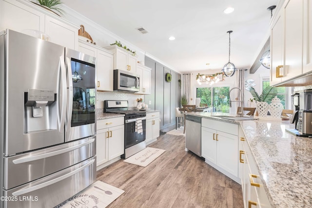 kitchen with sink, appliances with stainless steel finishes, white cabinetry, light stone counters, and decorative light fixtures