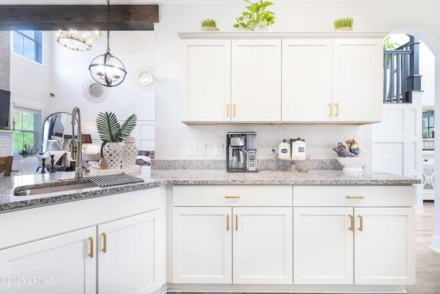 kitchen featuring white cabinets, sink, backsplash, and a chandelier