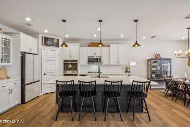 kitchen featuring stainless steel appliances, decorative light fixtures, a center island with sink, and white cabinets