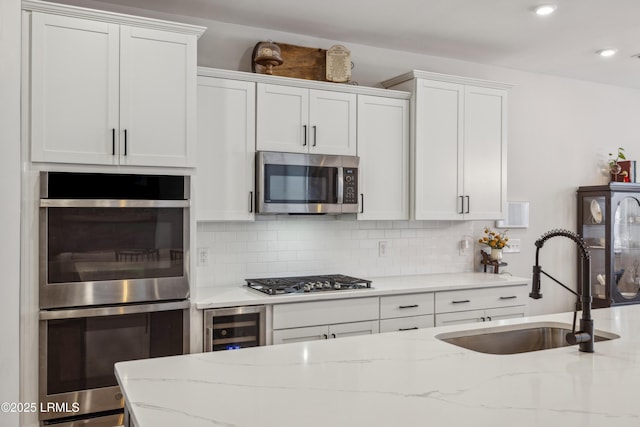 kitchen with stainless steel appliances, white cabinetry, light stone countertops, and sink