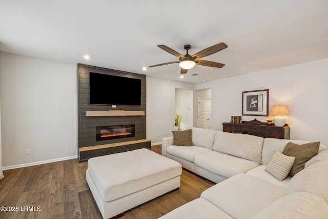 living room with ceiling fan, a large fireplace, and wood-type flooring