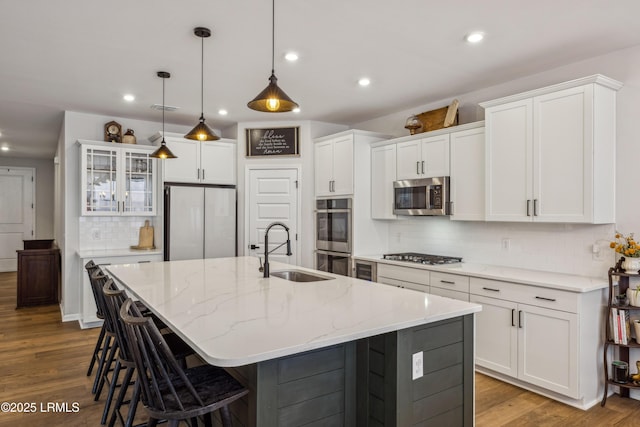 kitchen with sink, white cabinetry, hanging light fixtures, stainless steel appliances, and a center island with sink