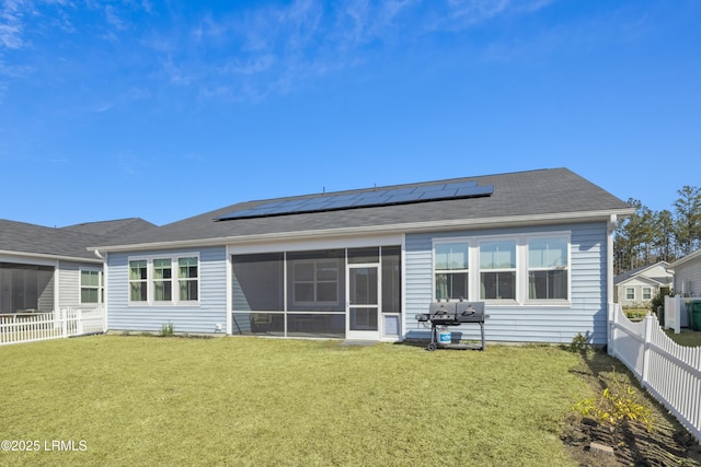 back of property with a sunroom, a yard, and solar panels