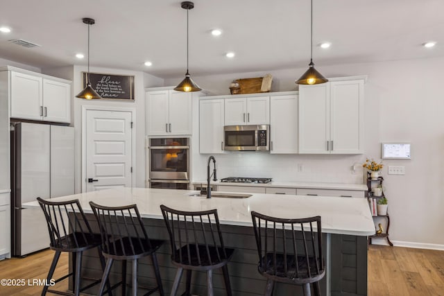 kitchen with appliances with stainless steel finishes, hanging light fixtures, a center island with sink, and white cabinets