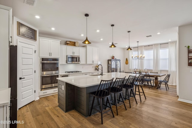 kitchen featuring sink, a breakfast bar, appliances with stainless steel finishes, white cabinetry, and an island with sink