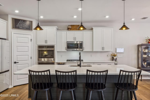 kitchen with white cabinetry, decorative light fixtures, a kitchen island with sink, and appliances with stainless steel finishes