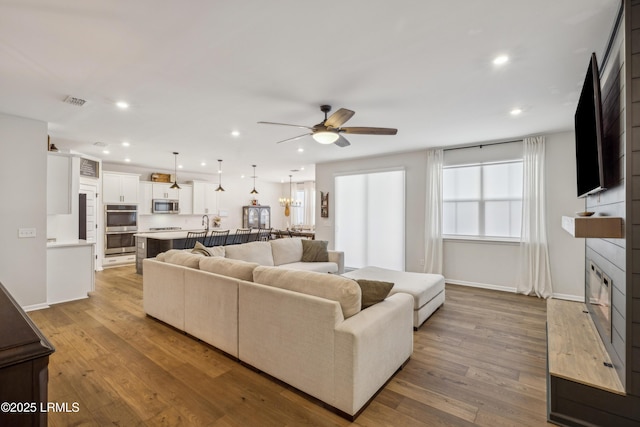 living room featuring light hardwood / wood-style flooring, a large fireplace, and ceiling fan