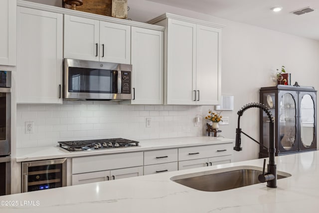 kitchen featuring sink, appliances with stainless steel finishes, light stone counters, white cabinets, and beverage cooler