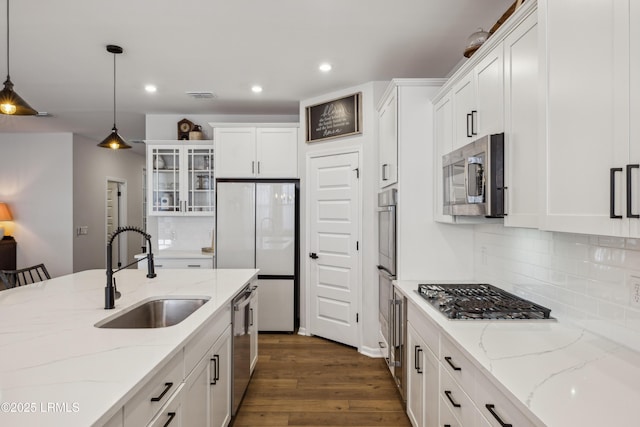 kitchen with appliances with stainless steel finishes, pendant lighting, sink, white cabinets, and light stone countertops