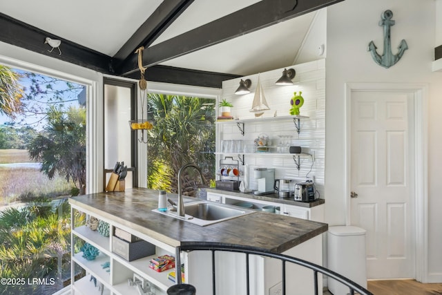 kitchen featuring vaulted ceiling with beams, butcher block countertops, a sink, and open shelves