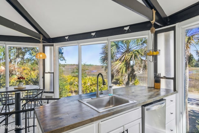 kitchen with lofted ceiling, wood counters, hanging light fixtures, white cabinetry, and a sink