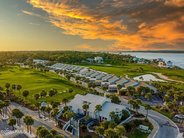 aerial view at dusk featuring view of golf course and a water view