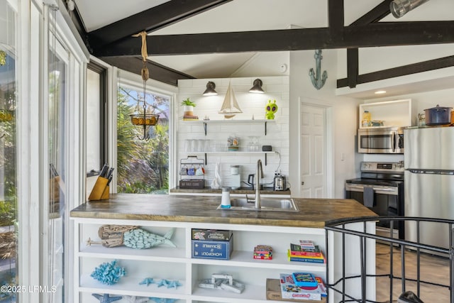 kitchen featuring open shelves, lofted ceiling with beams, appliances with stainless steel finishes, a sink, and wood counters