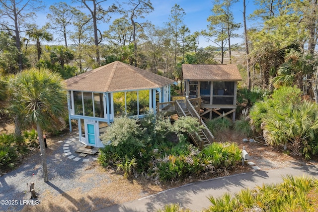 raised beach house with stairs, driveway, a shingled roof, and a sunroom