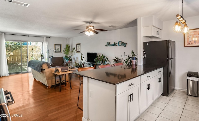 kitchen with white cabinetry, black fridge, decorative light fixtures, and a breakfast bar area