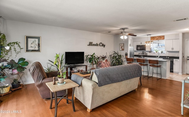 living room with sink, a textured ceiling, ceiling fan, and light wood-type flooring