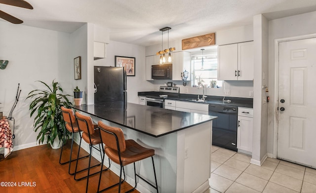 kitchen featuring white cabinets, a kitchen breakfast bar, hanging light fixtures, and black appliances