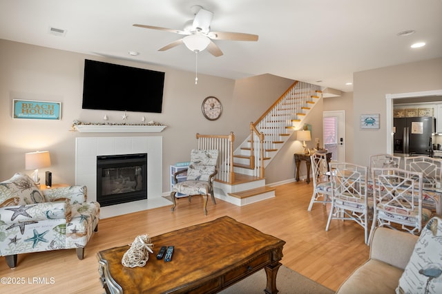 living area with stairway, a ceiling fan, wood finished floors, a tile fireplace, and recessed lighting