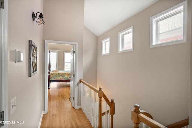 hall with vaulted ceiling, baseboards, light wood-style flooring, and an upstairs landing
