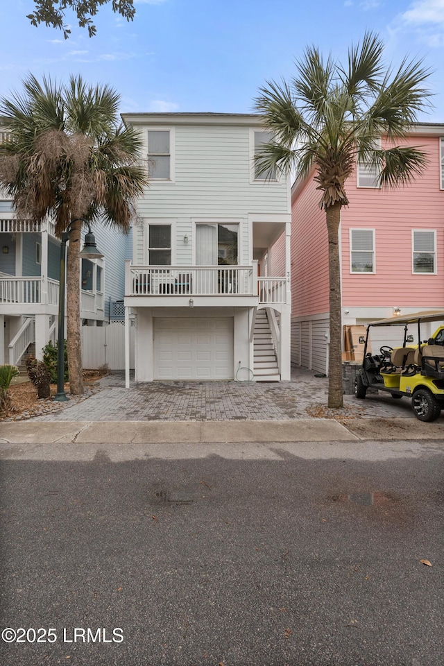 coastal home with a garage, driveway, stairway, and fence