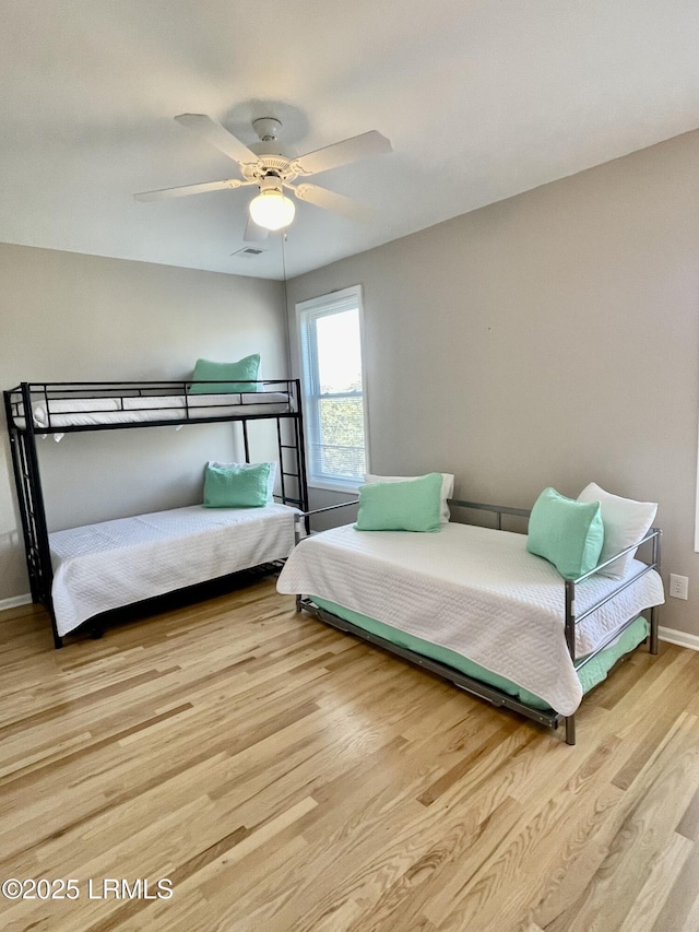 bedroom with wood finished floors, visible vents, a ceiling fan, and baseboards