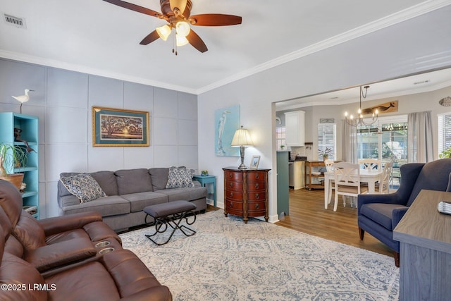 living room featuring ornamental molding, light wood-type flooring, visible vents, and ceiling fan with notable chandelier