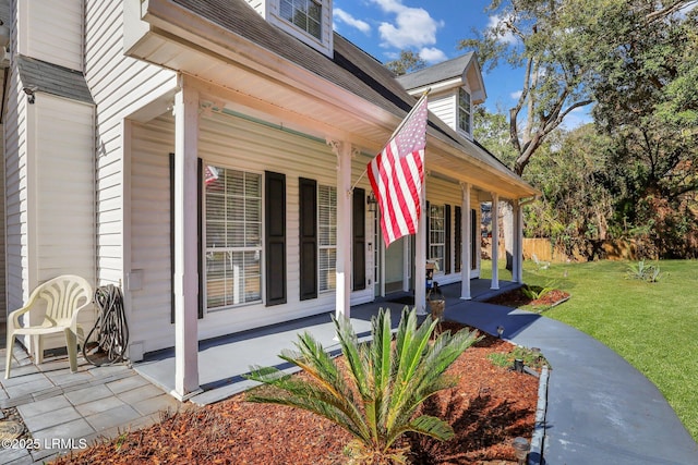 view of side of property with covered porch, a yard, a shingled roof, and fence