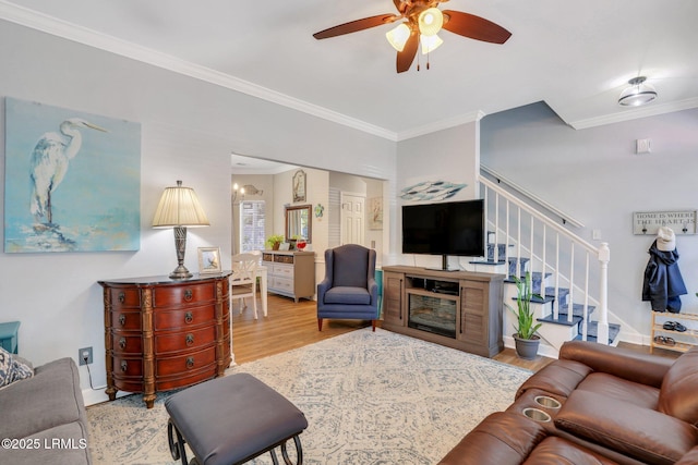 living room with a ceiling fan, crown molding, stairway, and wood finished floors