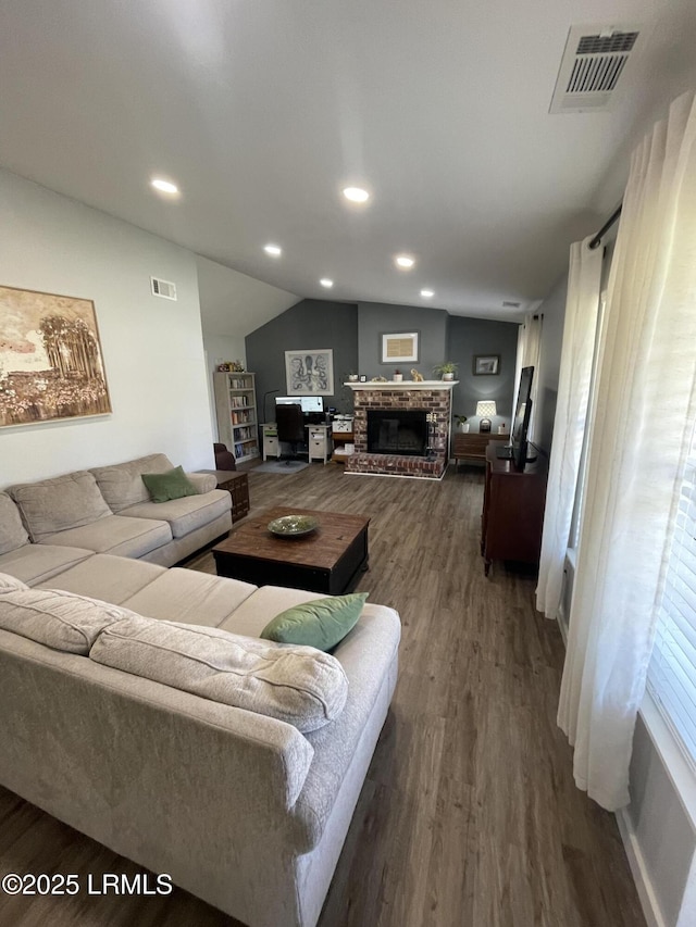 living room with dark wood-type flooring, vaulted ceiling, and a brick fireplace