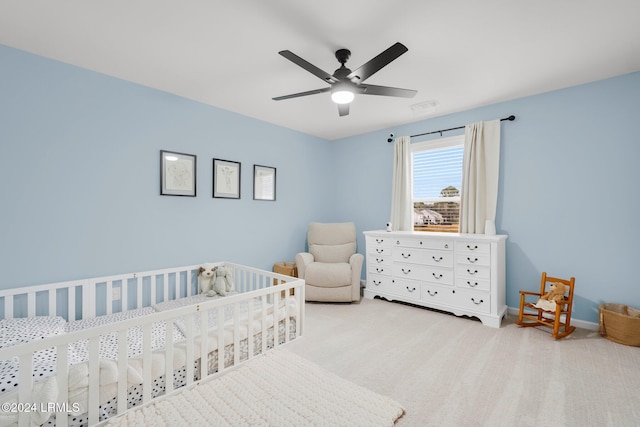 bedroom featuring a nursery area, light carpet, and ceiling fan