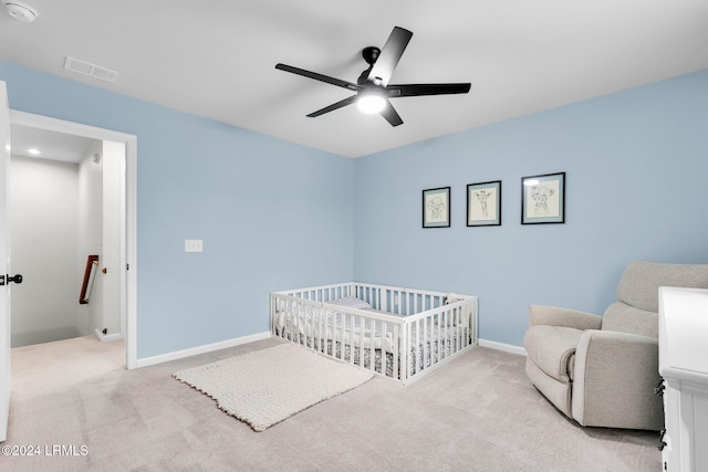 carpeted bedroom with a crib and ceiling fan