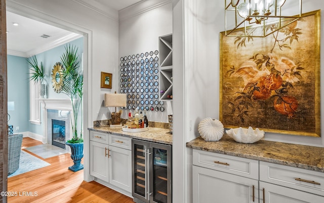 bar featuring wine cooler, light wood-style flooring, a dry bar, decorative light fixtures, and crown molding