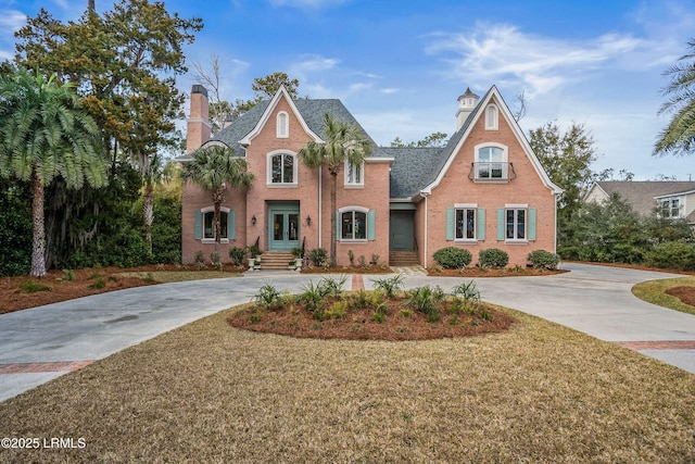 view of front facade with concrete driveway, brick siding, a chimney, and a front lawn