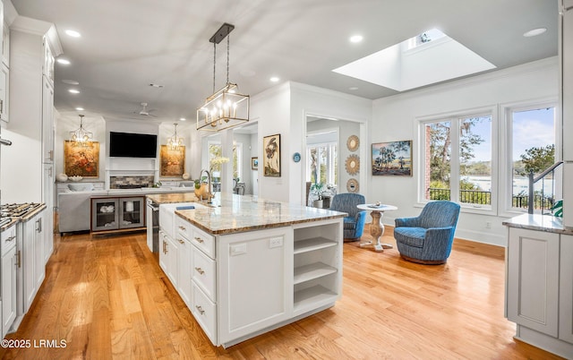 kitchen featuring white cabinets, an island with sink, light stone counters, open floor plan, and hanging light fixtures