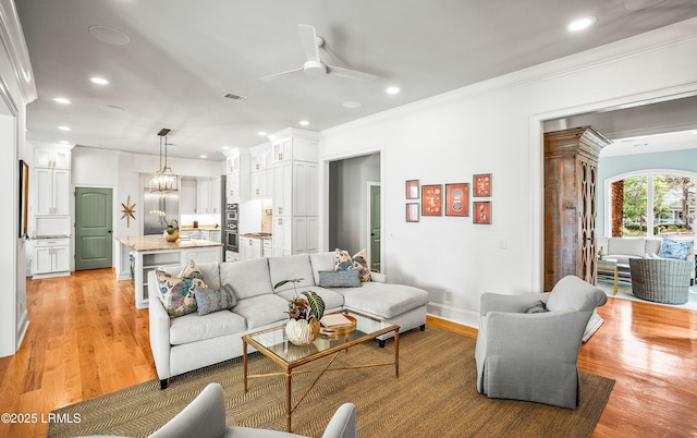 living area featuring light wood-type flooring, recessed lighting, visible vents, and ornamental molding