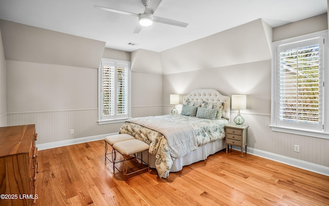 bedroom with lofted ceiling, visible vents, light wood-style flooring, wainscoting, and ceiling fan