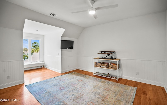 interior space featuring a ceiling fan, visible vents, wood finished floors, and wainscoting