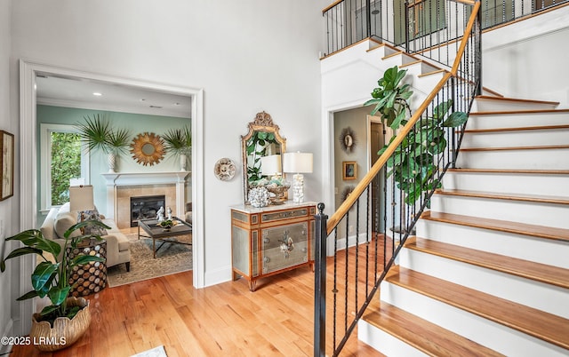 staircase featuring a high ceiling, a tiled fireplace, wood finished floors, and baseboards