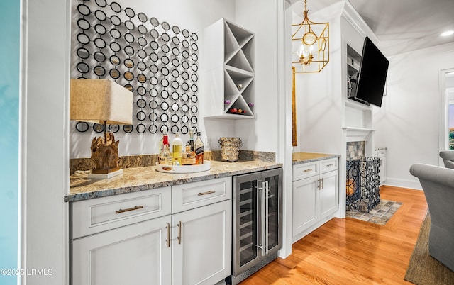 bar featuring light wood finished floors, beverage cooler, decorative light fixtures, crown molding, and a bar