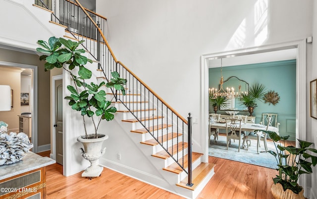 stairway with baseboards, a towering ceiling, an inviting chandelier, and wood finished floors