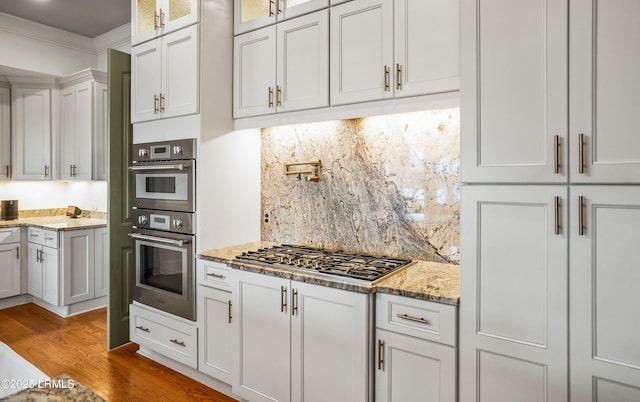 kitchen with light wood finished floors, white cabinets, appliances with stainless steel finishes, glass insert cabinets, and ornamental molding