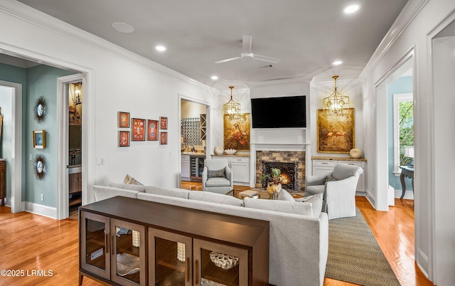 living room with light wood-style flooring, recessed lighting, crown molding, and a stone fireplace